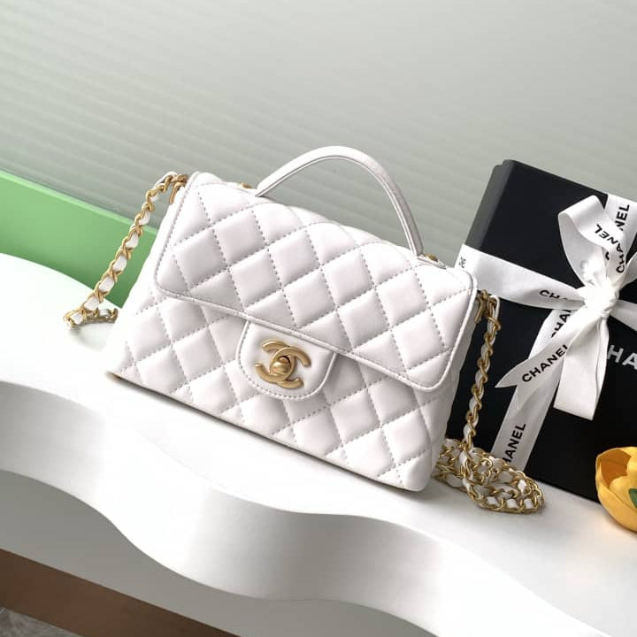 White quilted handbag with gold chain and clasp on a white surface with a black box featuring a white ribbon.