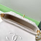 Close-up of a Chanel handbag with gold chain detail on a green surface.