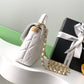 White quilted handbag with gold chain and black Chanel box with white ribbon on a white surface.
