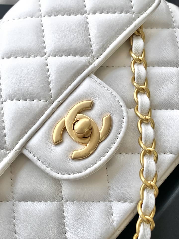White quilted handbag with gold chain and logo on a black background
